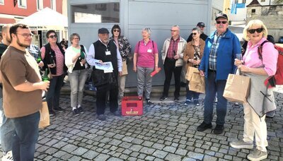 „Bier-Hopping durch Sulzbach-Rosenberg: Mehr als nur ein Schluck Geschichte!“ Sulzbach-Rosenberg, 23. April – Die Sonne schien, und die ersten Bierfreunde versammelten sich am Luitpoldplatz, um an der beliebten Führung von KulturAS teilzunehmen. Wer dachte, hier dreht sich alles nur um Bier, wurde schnell eines Besseren belehrt: Neben jeder Menge frisch gezapften Bieren gab es auch eine Vielzahl an Anekdoten und Geschichten, die für so manches Schmunzeln sorgten. Veranstalter Walter Heldrich hieß die Gruppe am historischen Löwenbrunnen willkommen. Gemeinsam mit den Gästeführern Monika und Peter Preller begab sich die Truppe auf eine kurzweilige Zeitreise durch die jahrhundertealte Braukultur der Stadt. Zum Auftakt erhielt jeder ein funkelndes Bierglas – und direkt am Platz wurde das erste „Fuchsbeck“-Bier verkostet. Anschließend erzählten die Prellers von der Blütezeit der Sulzbacher Brauereien. Erste Station war der Sperber Bräu: Dort erklärte der diplomierte Biersommelier Michael Sperber bei einer Zoigl Verkostung, wie die Spezialitäten der Brauerei nach dem „Reinheitsgebot“ gebraut werden und wie die Brauerei für die Zukunft aufgestellt wird. Auf dem weiteren Weg durch die Altstadt führte die Tour an den einstigen Bierlieferanten Schinhammer, an der Bäckerei & Bierschenke Kreiner, am Tucherdepotstüberl und am Ratskeller vorbei. Peter Preller ließ die Geschichten der verschwundenen Schänken lebendig werden und machte deutlich, wie eng die Orte einst mit dem gesellschaftlichen Leben verwoben waren. Im „Bayerischen Hof“, einer ehemaligen Brauerei, gewährte Gastgeber Georg Eberwein Einblicke in fast 200 Jahre Familiengeschichte. Er spannte den Bogen von den Gründergenerationen Renner und Seitz bis zur heutigen Familie Eberwein und zeigte, wie Familientradition und handwerkliches Können die Braukunst über Jahrzehnte prägten. Anschließend führte der Weg die Gruppe weiter zur Fuchsbeck-Brauerei, und nach nur wenigen Schritten bestaunte man das mächtige 12 Hektoliter Fass. Peter Preller erläuterte, wie die Familie Fuchs 1820 von der Bäckerei zum Brauhaus wechselte und das Braurecht später an die Familie Orth überging. Den krönenden Abschluss bildete das Gasthaus „Zur Landkutsche“ (Pamler-Wirtschaft) an der alten Nürnberger Straße, wo Christian Kellner von der Gründung um 1400, dem Brand im Landshuter Erbfolgekrieg 1504 und dem Wiederaufbau im späten 16. Jahrhundert berichtete. Heute lockt ein schattiger Biergarten unter Kastanien, während drinnen ein König-Ludwig-Bild für urige Stimmung sorgt. Drei Kanonenkugeln mit der Inschrift MCCCC A.D. und eine Johannes Nepomuk-Statue an der Tür erinnern an das mittelalterliche Erbe. Organisator Walter Heldrich dankte abschließend allen Mitwirkenden – insbesondere Martina Heiß, da die Landkutsche normalerweise nur Freitags geöffnet ist, extra für den Ausklang öffnete. Der Erlös der Führung kommt einer regionalen Wohltätigkeitsorganisation zugute. Mit kurzweiligen Anekdoten, informativen Einblicken und frisch gezapften Bieren bot die Führung zum Tag des Bieres einen rundum gelungenen Streifzug durch die Biergeschichte Sulzbach Rosenbergs. Prost!